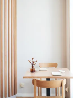 Lyst tr&aelig;bord med to stole, sm&aring; hvide serveringsfade og en lille vase hos Izumi i et minimalistisk nordisk-japansk interi&oslash;r.