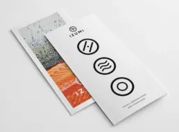 Izumi brochure mockup med hvide omslag, sorte minimalistiske ikoner og et billede af frisk laks p&aring; den bageste forside.