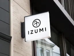 Izumi restaurant facadeskilt med logo og typografi p&aring; bygningens yderside.