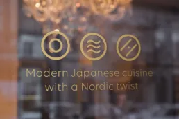 Guldikoner fra Izumis visuelle identitet p&aring; glasfacaden, med teksten &ldquo;Modern Japanese cuisine with a Nordic twist&rdquo;.