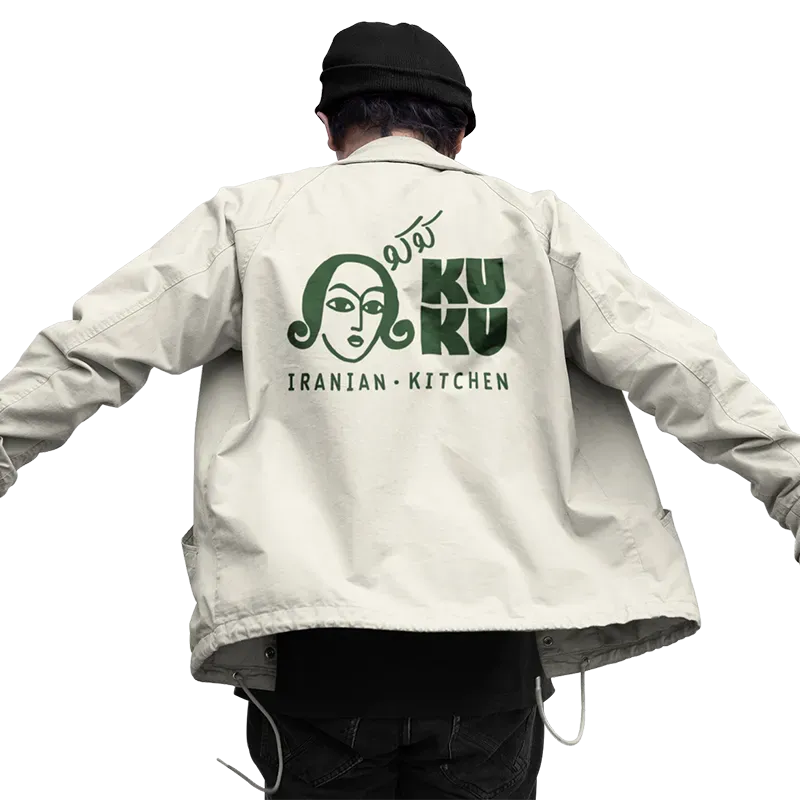 Person if&oslash;rt beige jakke med KUKU Iranian Kitchen logo trykt p&aring; ryggen.