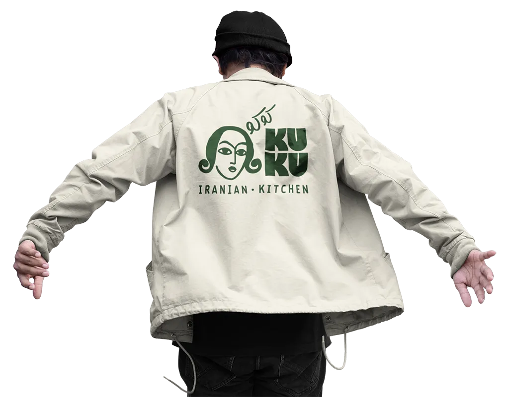 Person if&oslash;rt beige jakke med KUKU Iranian Kitchen logo trykt p&aring; ryggen.