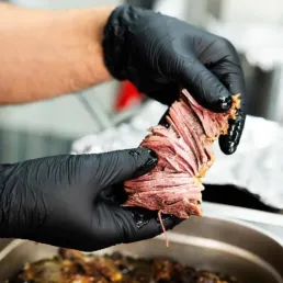 Kok med sorte handsker river langtidsbraiseret k&oslash;d fra KUKU Iranian Kitchen i K&oslash;benhavn.