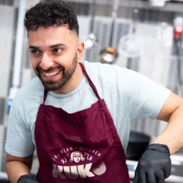 KUKU Iranian Kitchen &ndash; medarbejder i k&oslash;kkenet if&oslash;rt forkl&aelig;de med logo designet af Comugraph.