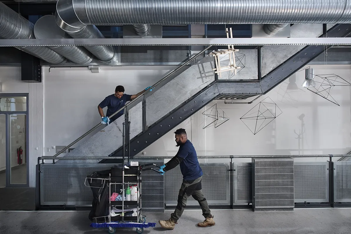 To medarbejdere fra Rengoering.com udf&oslash;rer professionel reng&oslash;ring i en moderne industribygning med st&aring;ltrapper og ventilationsr&oslash;r. Billedet viser virksomhedens fokus p&aring; kvalitet og teamwork.
