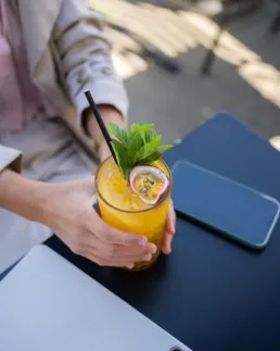 Hånd holder et glas med friskpresset juice pyntet med mynte og passionsfrugt på Social Brew caféens udendørsområde.