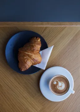 Kaffe og croissant serveret på træbord hos Social Brew café, set oppefra i et minimalistisk skandinavisk design.
