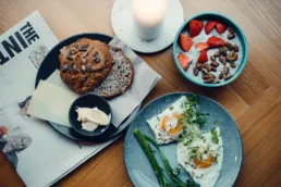 Morgenmad hos Social Brew med chia bowl, spejlæg, brød, ost og smør serveret på træbord i hyggelig caféstemning.