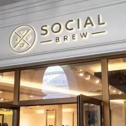 Social Brew café facade med oplyst logo over indgangen, designet i moderne og minimalistisk stil.