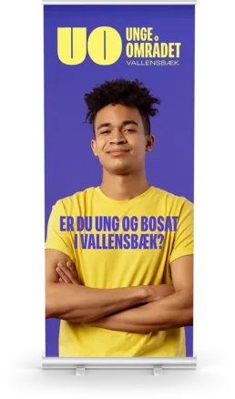 Ungeomr&aring;det roll-up banner med ung mand i gul t-shirt foran lilla baggrund og teksten &ldquo;Er du ung og bosat i Vallensb&aelig;k?&rdquo; &ndash; designet af Comugraph for Vallensb&aelig;k Kommune.