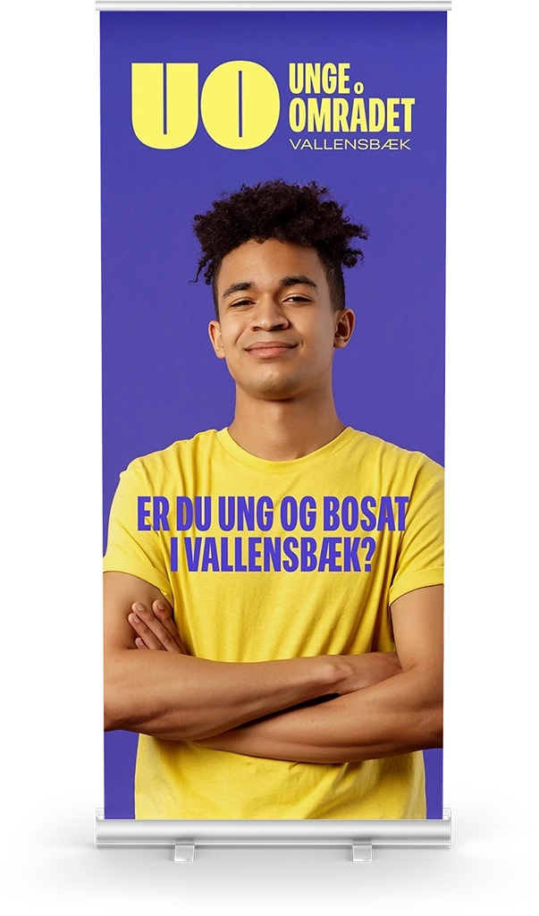 Ungeomr&aring;det roll-up banner med ung mand i gul t-shirt foran lilla baggrund og teksten &ldquo;Er du ung og bosat i Vallensb&aelig;k?&rdquo; &ndash; designet af Comugraph for Vallensb&aelig;k Kommune.